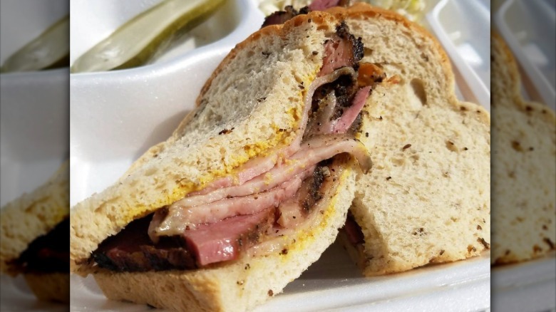 Close up of a pastrami sandwich with pickle on the side