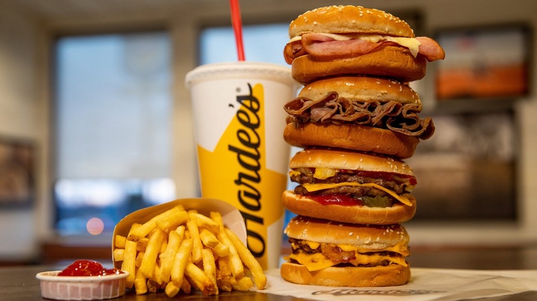 Four Hardee's sandwiches with fries, drink, and ketchup on restaurant table.
