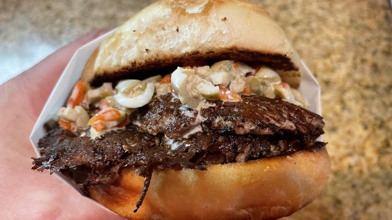 Hand holding Michigan-style olive burger in paper wrapper.