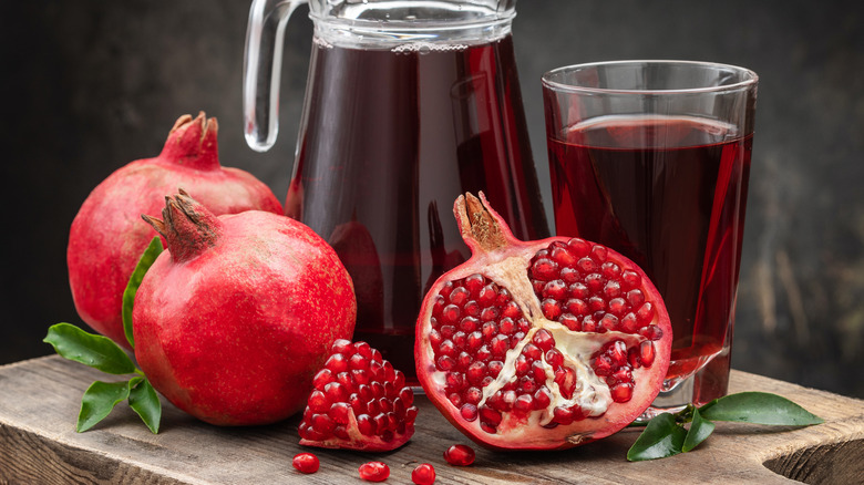 pomegranates, one is cut in half, jug and cup of pomegranate juice