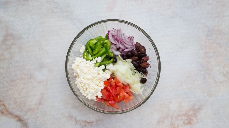 Various vegetables, feta cheese, and olives unmixed in bowl