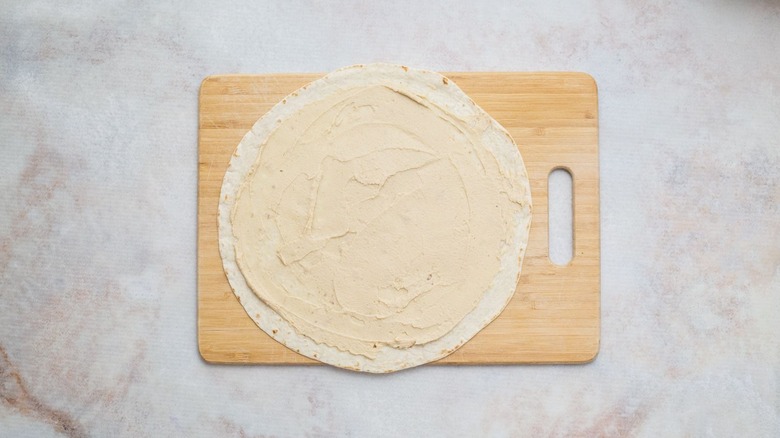 hummus spread across tortilla on wooden board