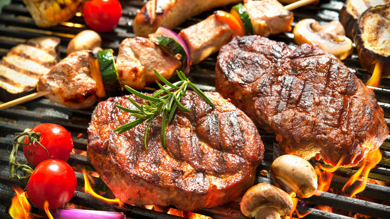 Two steaks, vegetables, and chicken skewers on a fiery grill