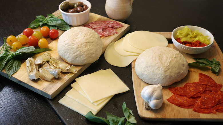 grilled antipasto pizza ingredients laid out on cutting boards on a dark wood table