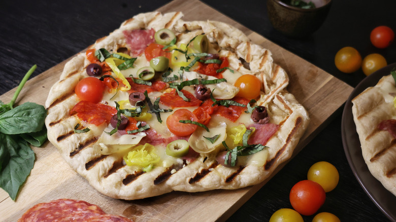overhead shot of grilled pizzas topped with salami, olives, cheese, pickled pepper, artichokes, and chiffonade basil