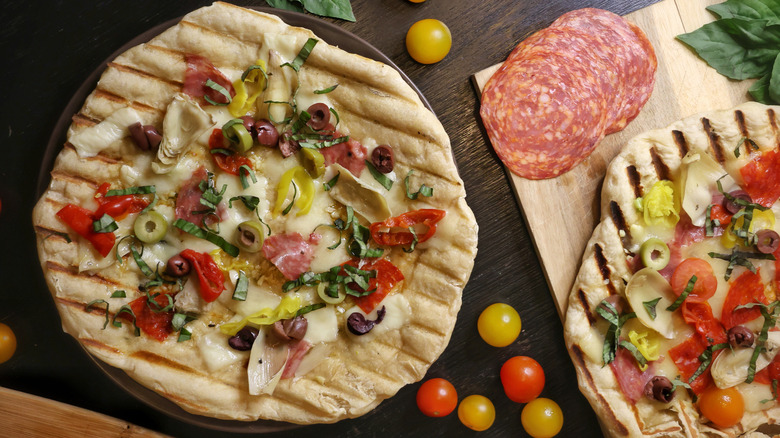 grilled pizzas topped with olives, artichokes, pickled peppers, salami, and chopped basil