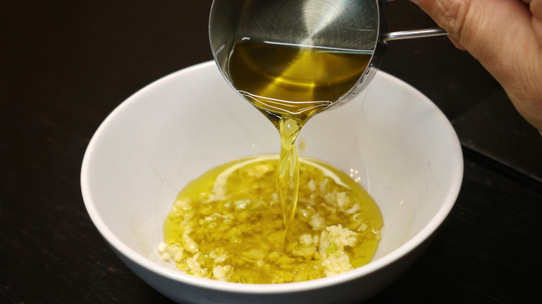 olive oil pouring from measuring cup into bowl of minced garlic