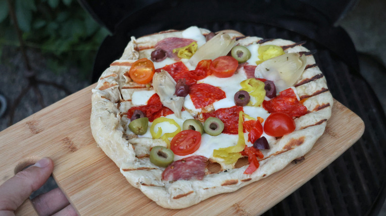 grilled pizza on a cutting board above a grill