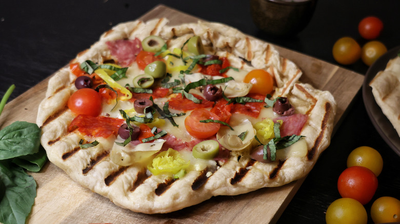grilled pizza topped with cherry tomatoes, olives, artichokes, pickled peppers, salami, and basil