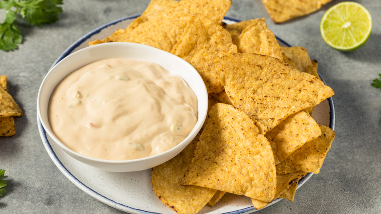 Bowl of light colored nacho cheese sauce with plate of tortilla chips