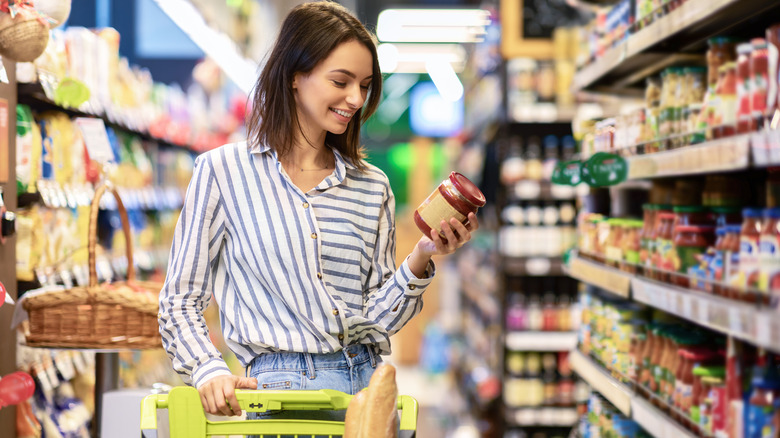 Woman holding a jar and pushing a grocery cart