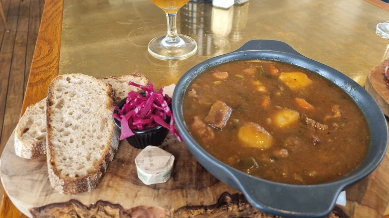 A bowl of lobscouse next to red cabbage and two slices of bread on a table in a restaurant