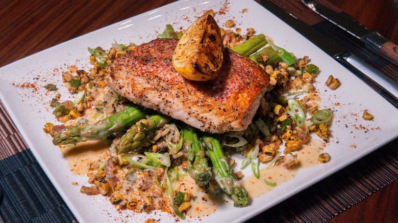 Seasoned fish and charred lemon wedge atop a bed of vegetables