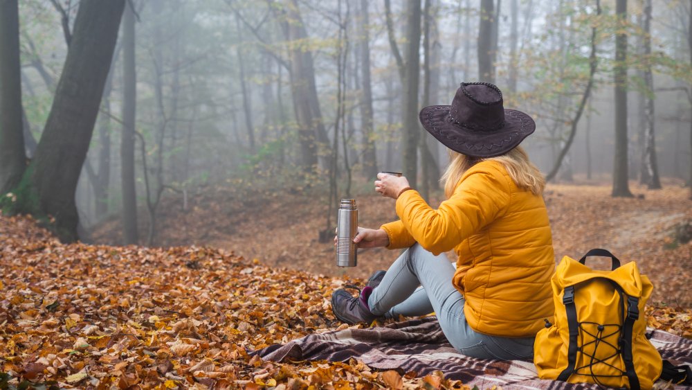 woman drinking coffee while camping in woods