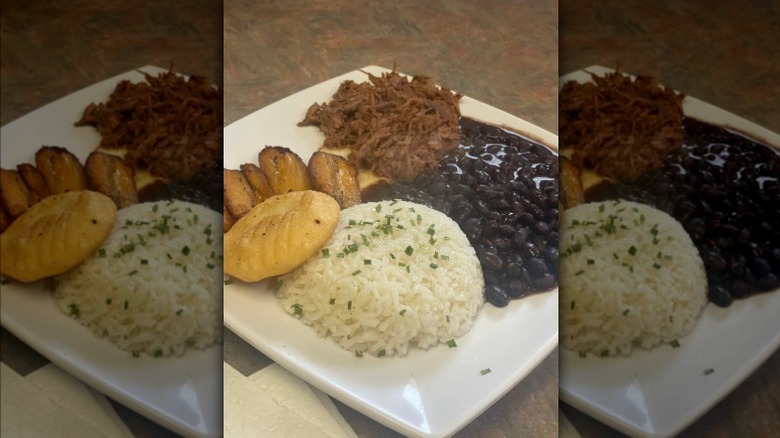Plate of black beans, rice, and fried plantains with arepa