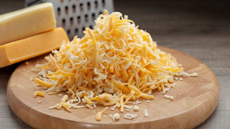 Pile of shredded cheese next to cheese block and grater