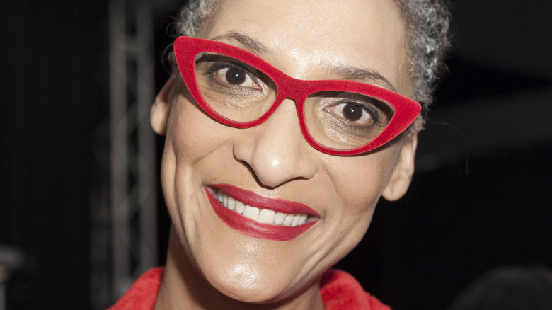 Carla Hall smiles with red glasses and red lipstick