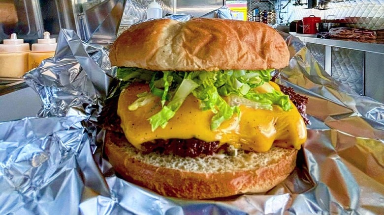 A cheeseburger on foil with lettuce