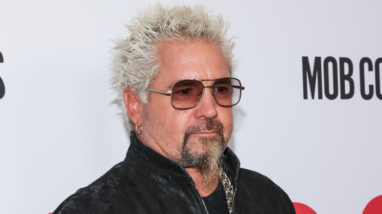 Guy Fieri headshot, wearing sunglass and his signature spiked hair at an event