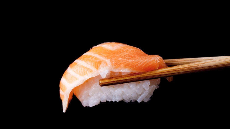 A pair of chopsticks holding salmon sushi