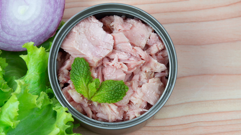 canned tuna on a wooden surface beside rd onion and lettuce