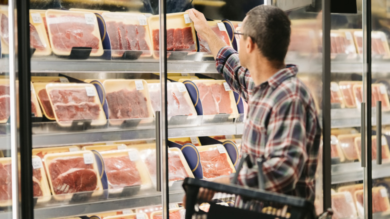 Customer with hand basket inspecting steak inside grocery store.