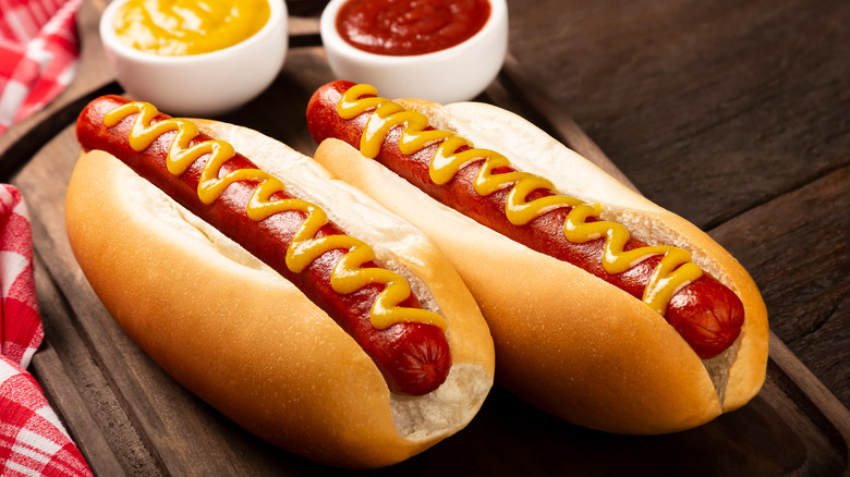 two hot dogs in buns topped with mustard and ketchup on the side