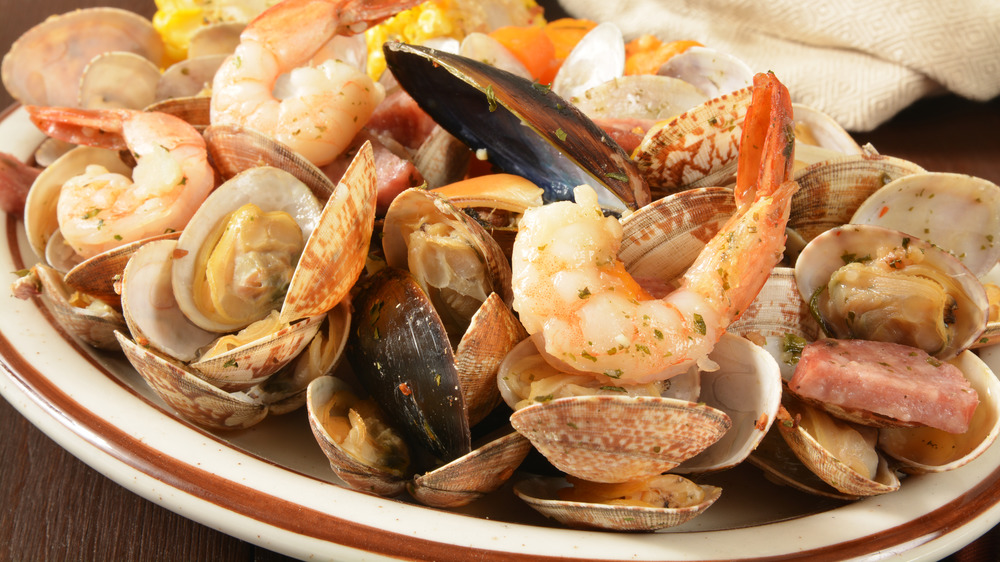 Closeup of New England style clambake with shrimp mussels, clams and sausage on white plate