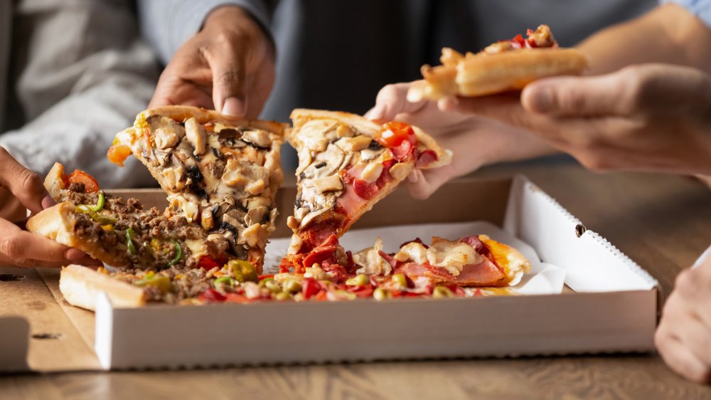 Hands reaching into pizza box grabbing slices of pizza 