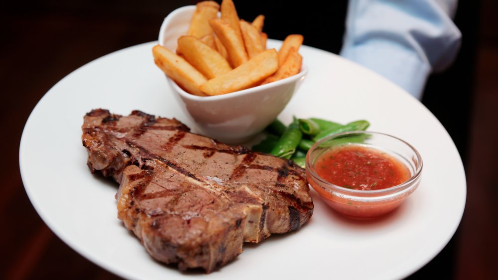 Waiter holding T-bone and french fries on a plate
