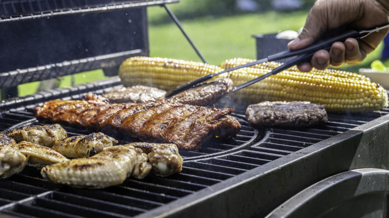 person using metal tongs to turn meat cooking on the frill