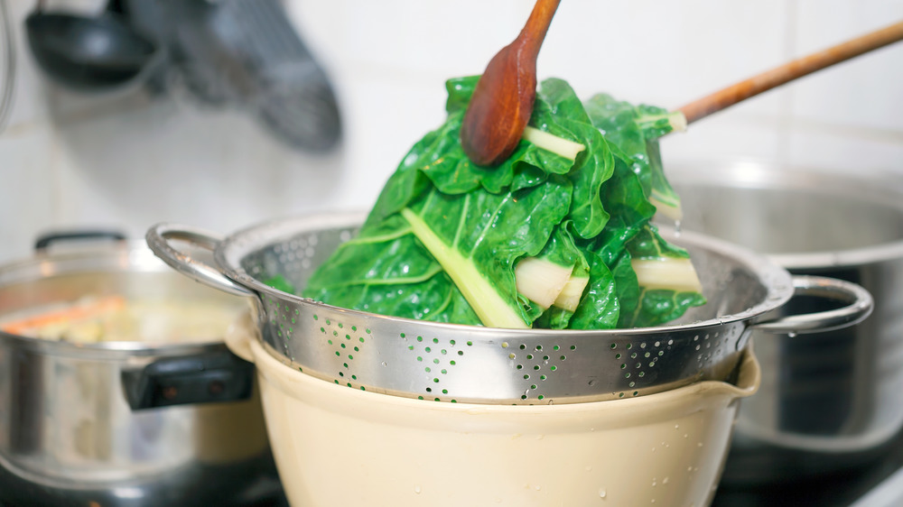 Blanching leafy greens over a pot on the stove