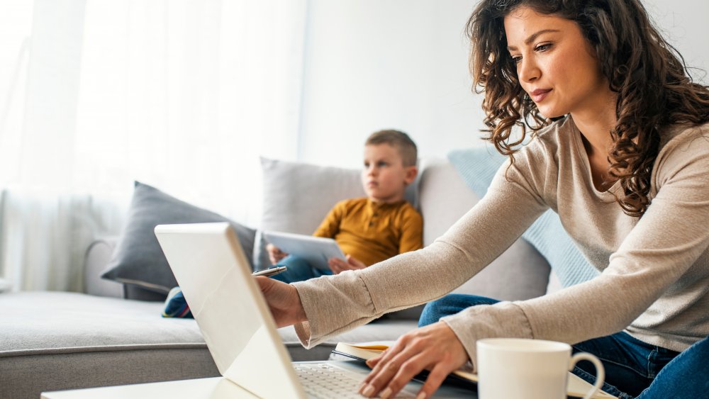 mom on laptop at home with young boy in background
