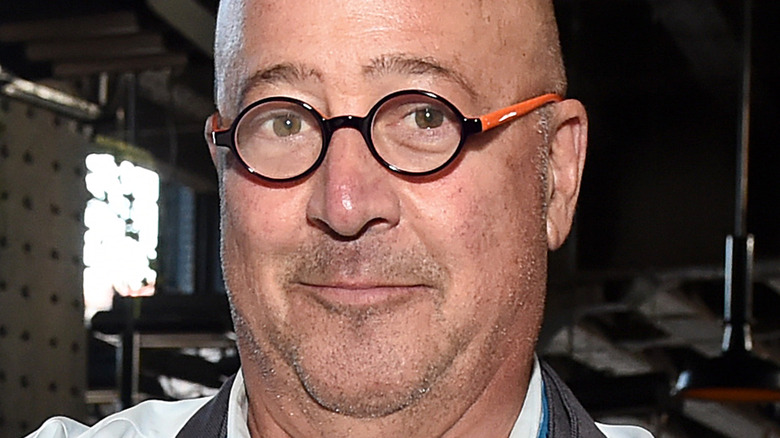 Andrew Zimmern wearing a white shirt, apron and glasses
