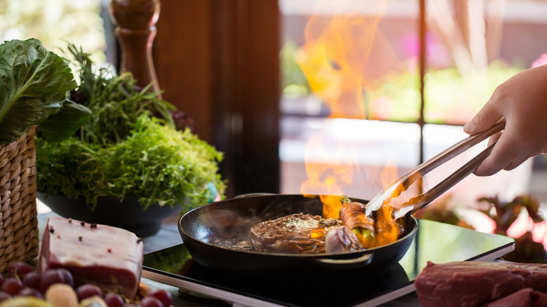 Hands with tongs turning a flambé steak