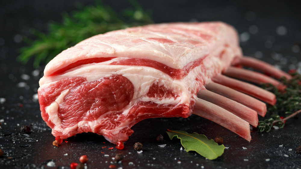 raw rack of lamb on black surface with peppercorns and bay leaf