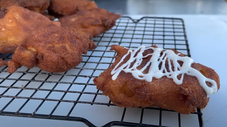 Apple fritters by Cowboy Kent Rollins on a wire rack, with one piece drizzled with cream