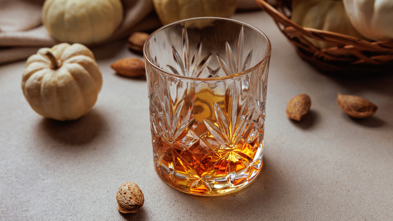 glass with whiskey surrounded by pumpkins