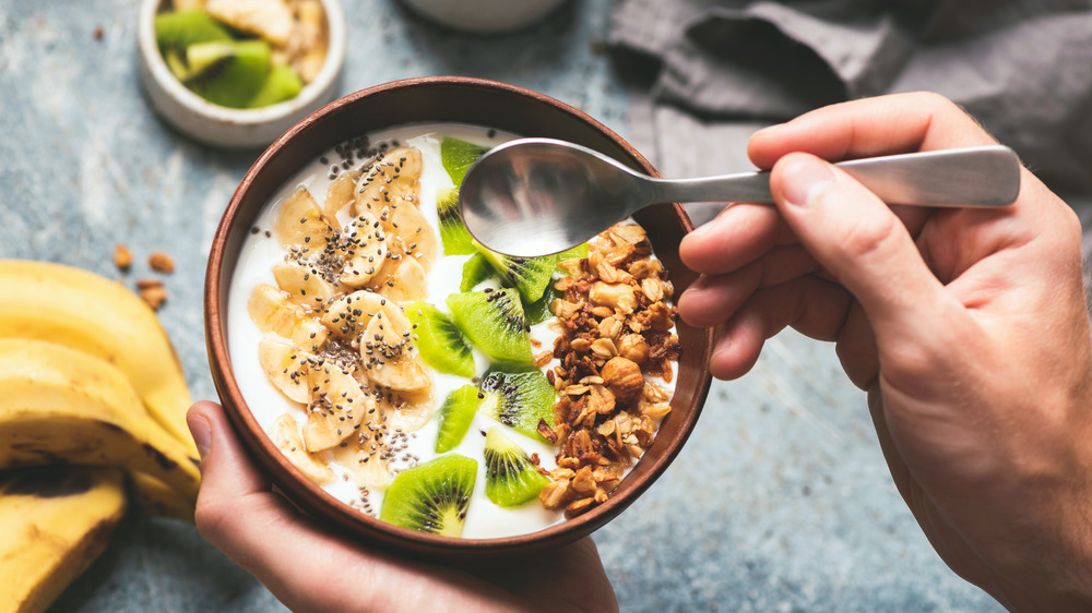 A person eating yogurt topped with fruits