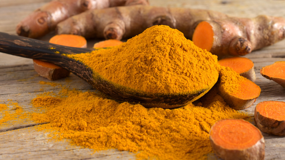 Ground turmeric on wooden spoon with root