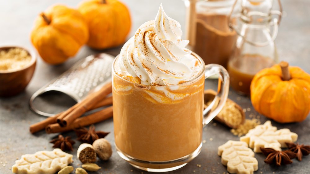 Pumpkin spice latte with whipped cream surrounded by pumpkins, cookies, and spices