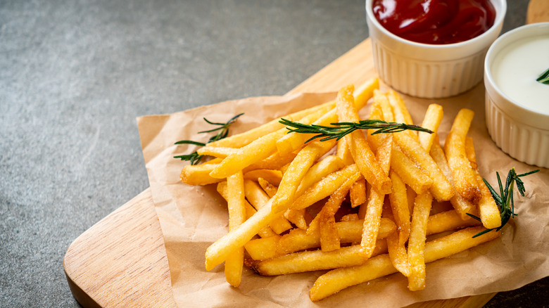 French fries and thyme atop a wooden board with two ramekins of dipping sauce