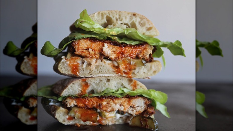 A stacked fried chicken sandwich on ciabatta bread with lettuce, pickles, and sauce that's dripping down the bread.