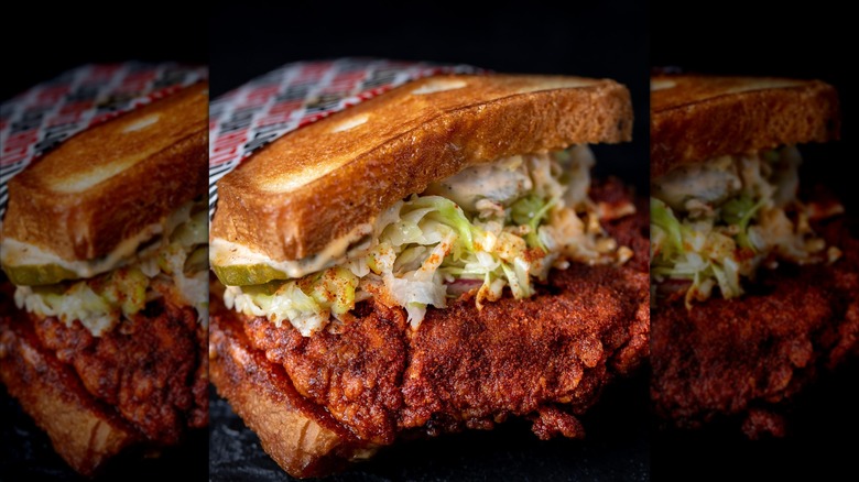 A fried chicken sandwich on toasted bread, piled with slaw, pickles, and creamy sauce.