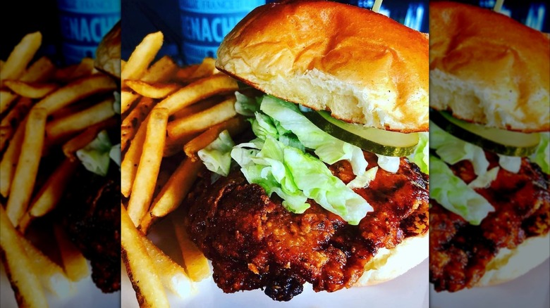 A close-up of a fried chicken sandwich with lettuce and pickles on a toasted bun, served with a side of fries.