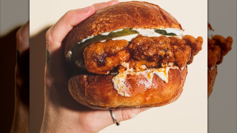 A hand holding a fried chicken sandwich with pickles and sauce on a toasted bun.