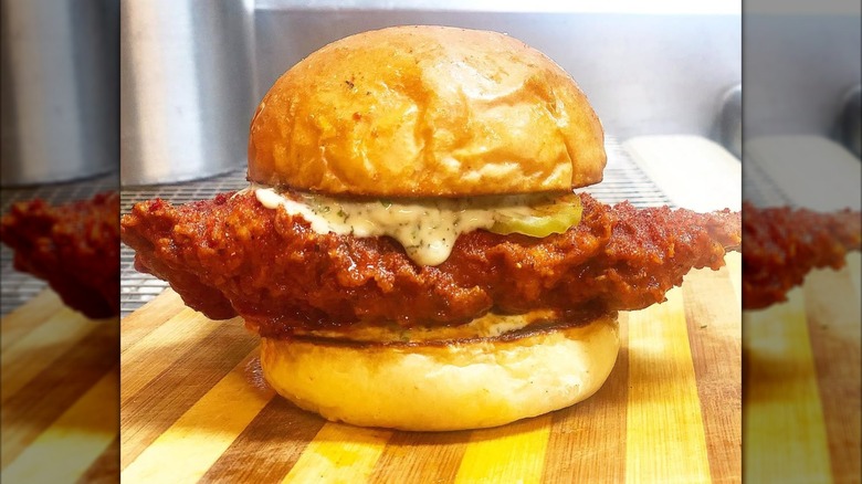 A fried chicken sandwich with a huge piece of chicken, pickles, and creamy sauce on a toasted bun.