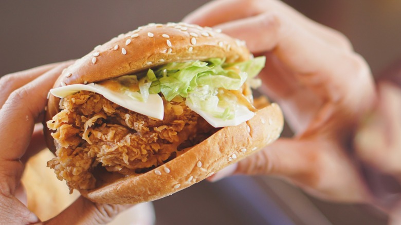 Someone holding a fried chicken sandwich with cheese and lettuce