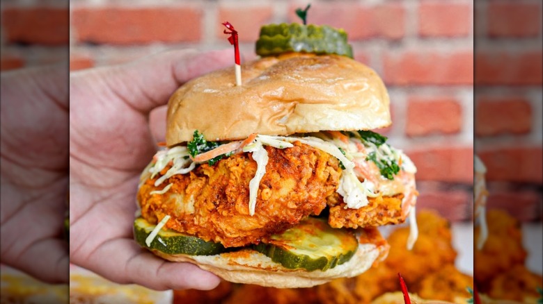 ​​Someone holding a fried chicken sandwich with pickles and a slaw