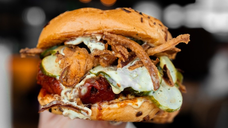 A fried chicken sandwich stacked with pickles, crispy onions, and a creamy sauce